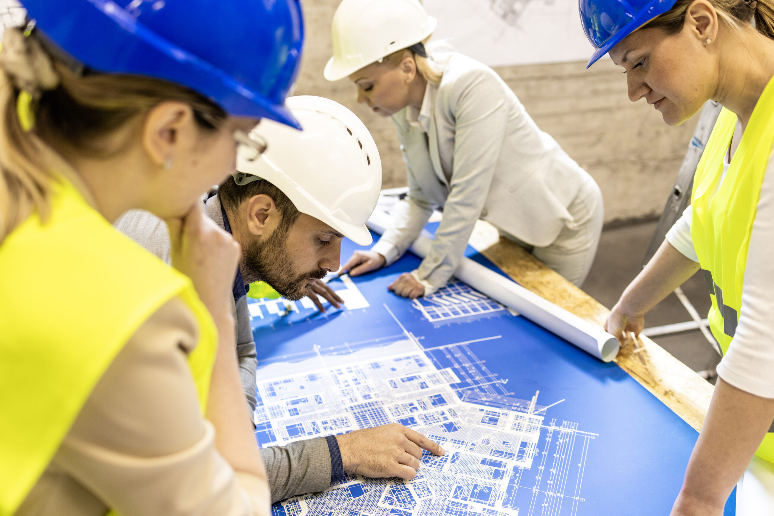 Top view of architects and engineers at construction site analyzing blueprint and project plan.